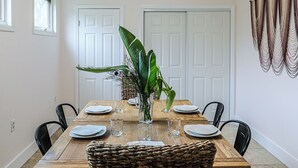 A dining room with a wooden table set for four, surrounded by black chairs. There are two white doors in the background, and a large green plant in a glass vase on the table. - Newly Renovated Home w/Outdoor Shower, Pool & Tiki Hut!  (Crystal River)