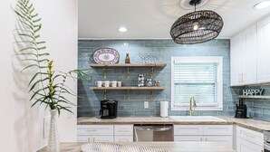 A modern kitchen with white cabinets, a blue tiled backsplash, and a hanging light fixture. - Newly Renovated Home w/Outdoor Shower, Pool & Tiki Hut!  (Crystal River)