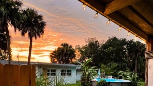 A view from a balcony with a wooden railing, overlooking a backyard with a swimming pool, a house, and palm trees. - Newly Renovated Home w/Outdoor Shower, Pool & Tiki Hut!  (Crystal River)