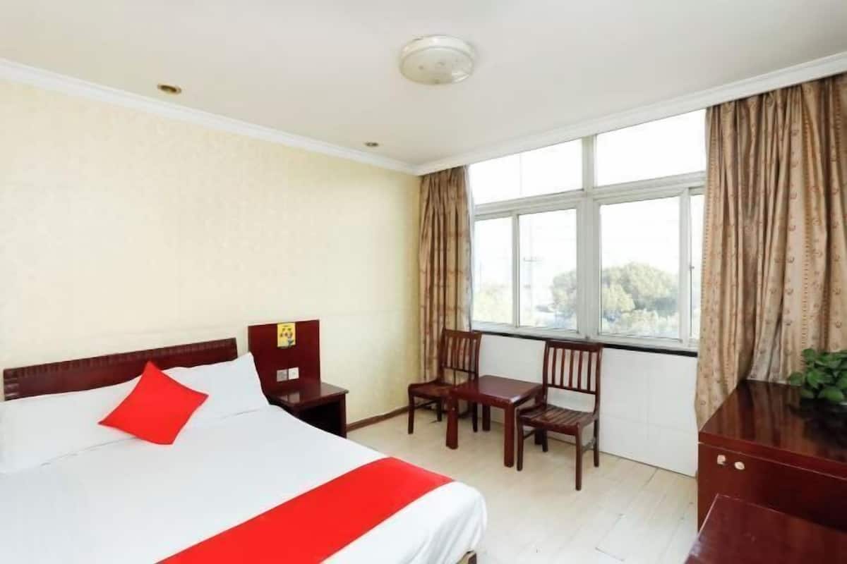 A hotel room with a bed, a desk, two chairs, and a window with curtains.