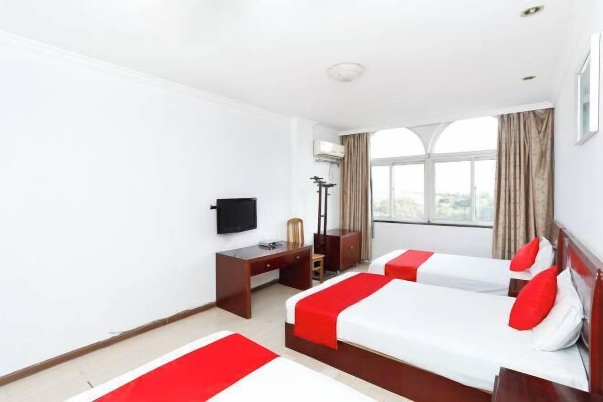 A hotel room with two beds, a desk, a chair, a TV, and a window with curtains.