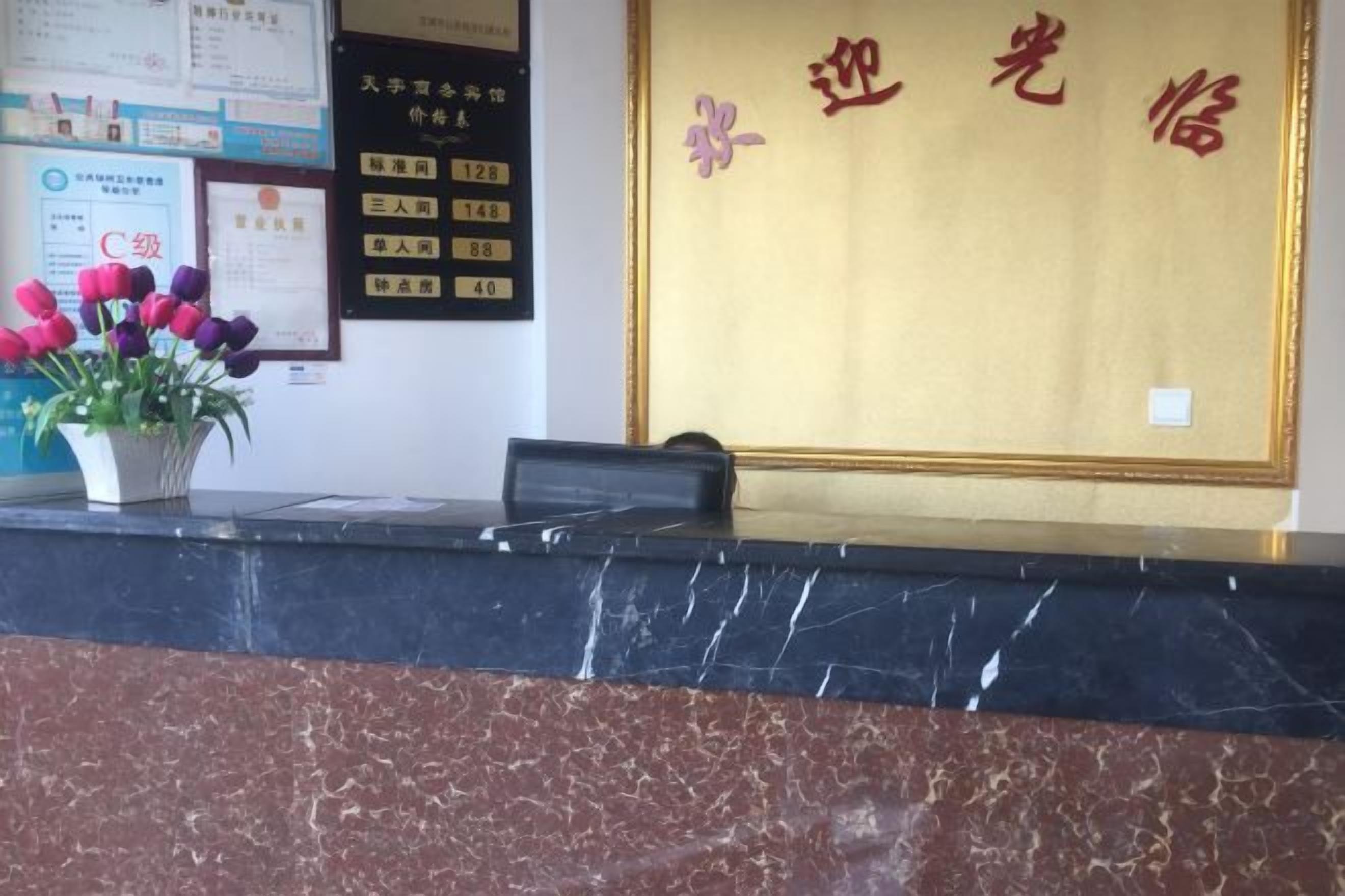 A reception desk with a marble top, a potted plant with flowers, and a wall with a framed certificate.