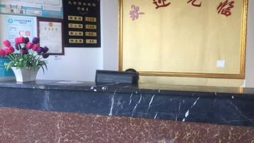 A reception desk with a marble top, a potted plant with flowers, and a wall with a framed certificate.