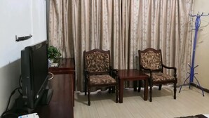 Una habitación con una televisión, dos sillas de madera, una mesita pequeña y un perchero.