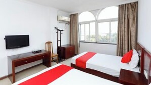 Habitación de hotel con dos camas, un escritorio, una silla, un televisor y una ventana con cortinas.