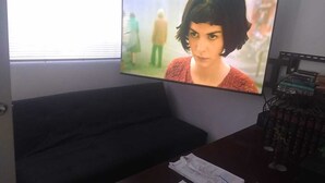 Een kamer met een donkergroene bank, een flatscreen televisie aan de muur en een klein tafeltje met enkele spullen erop.