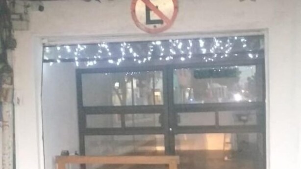Een gevel met een houten bank ervoor, een verbodsbord voor parkeren erboven en een lichtslingering boven de deur.