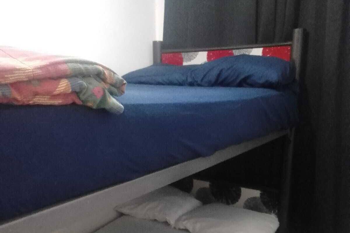 Una cama litera con un colchón azul y una litera inferior con un colchón blanco. Hay un taburete blanco pequeño al lado de la cama.