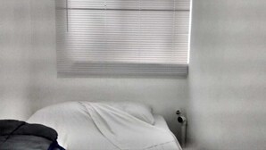 Een kamer met een bed, een raam met zonwering en een radiator.