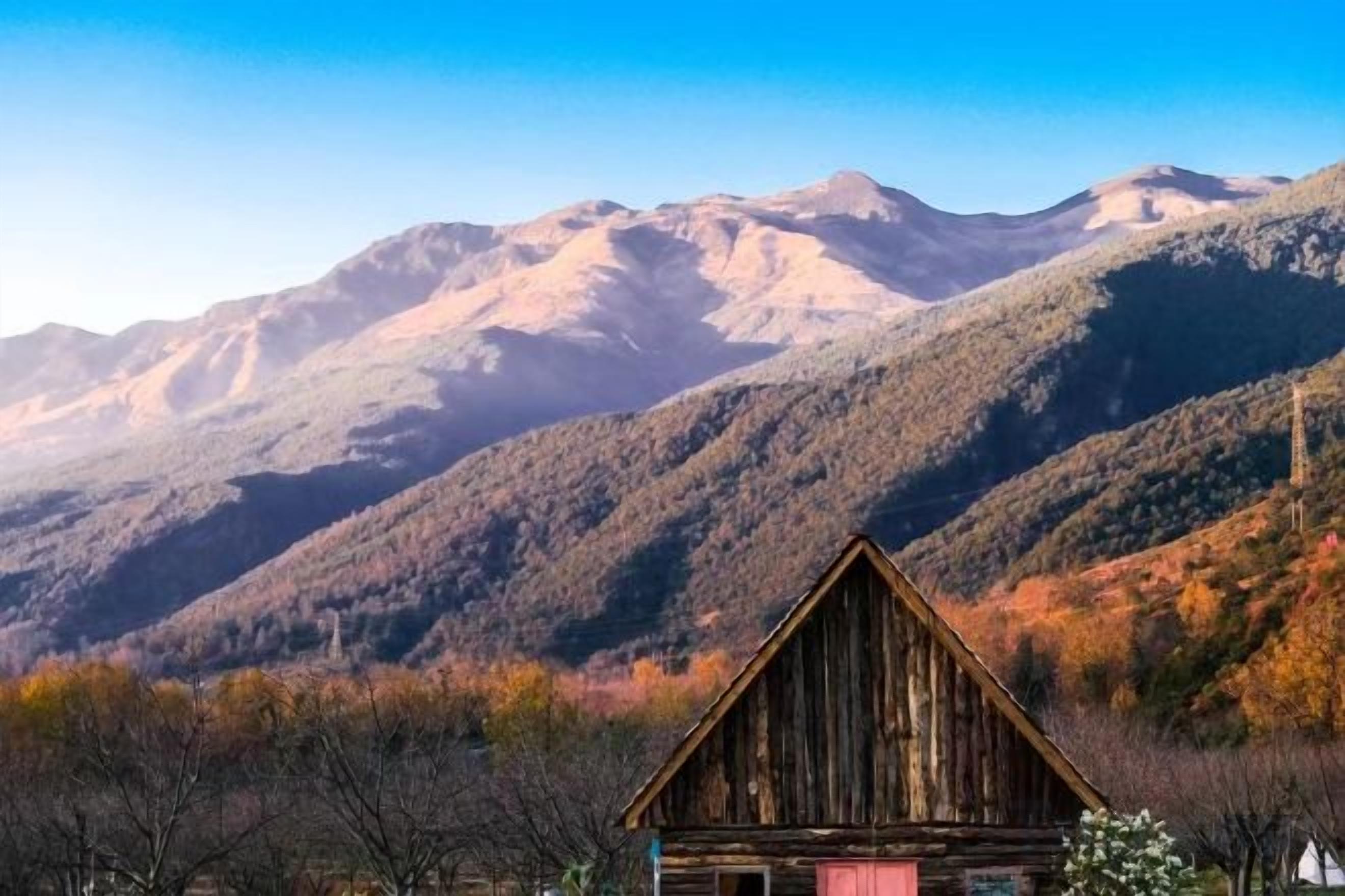 A rustic wooden cabin with a mountain backdrop.