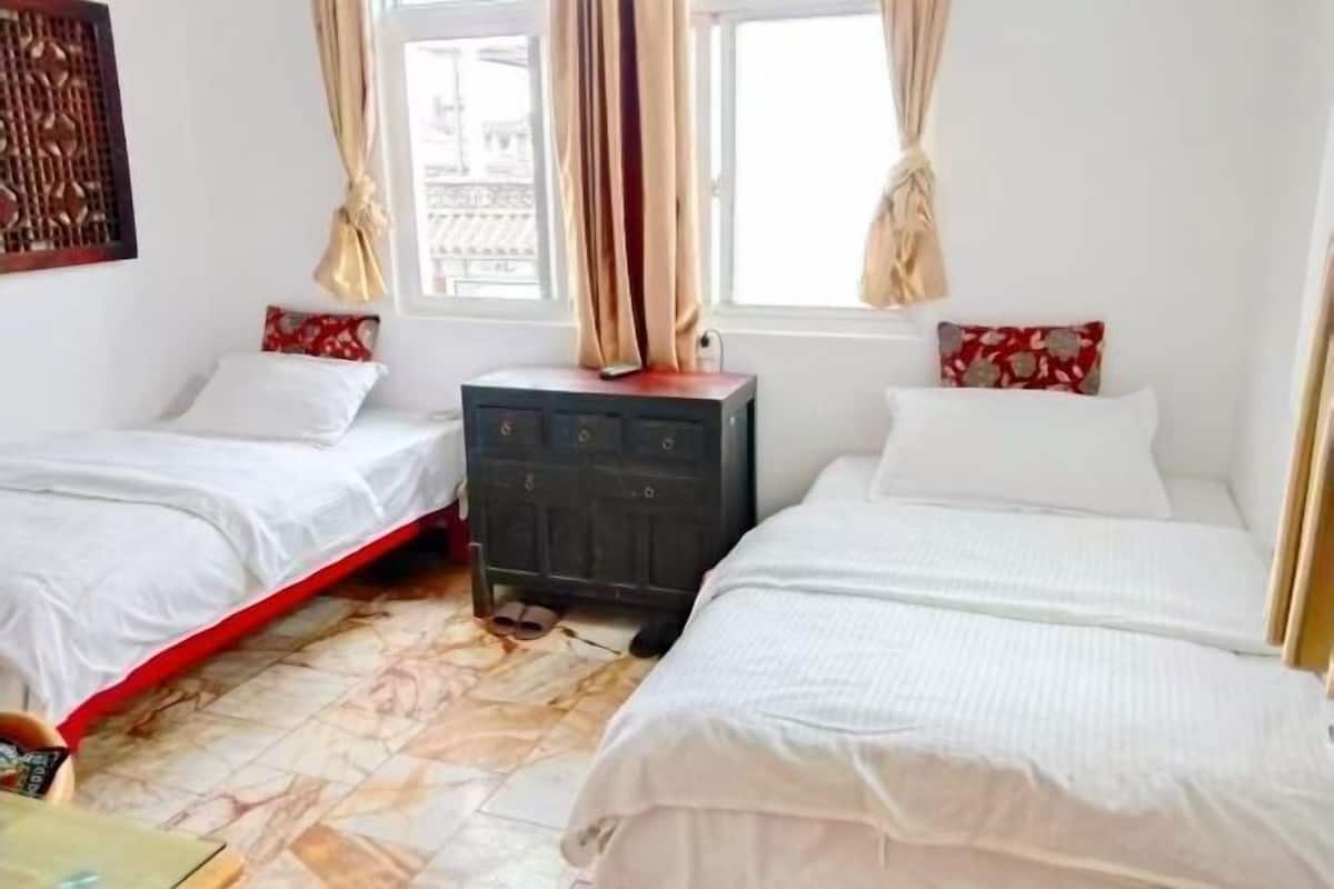 A room with two beds, a small cabinet, and a window with curtains.