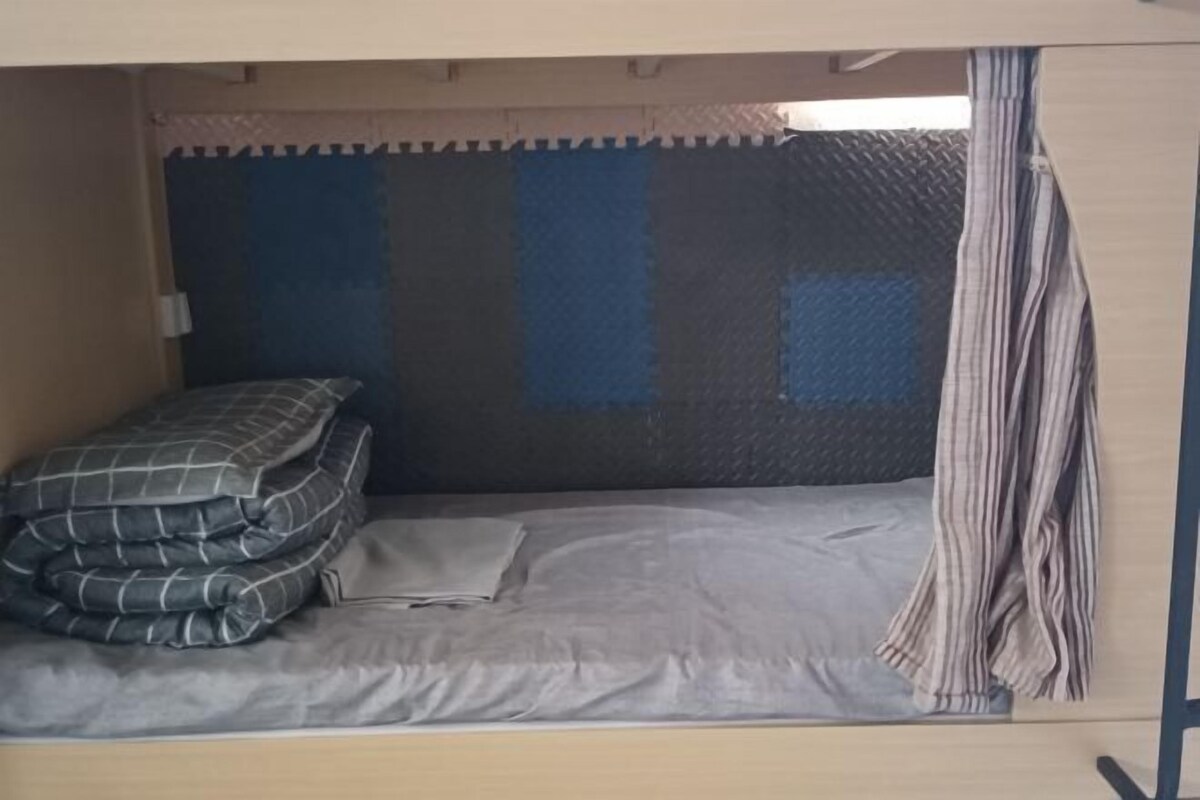 A bunk bed with a mattress and pillows, a striped curtain, and a headboard with a textured design.
