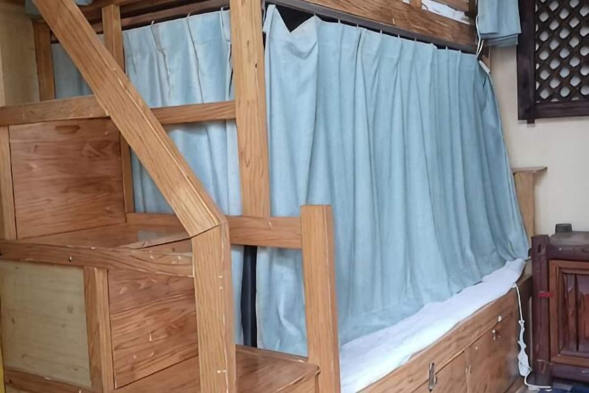 A wooden bunk bed with a curtain, a wooden cabinet, and a lattice window.