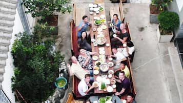 A group of people seated around a long wooden table outdoors with various dishes and a green bowl.