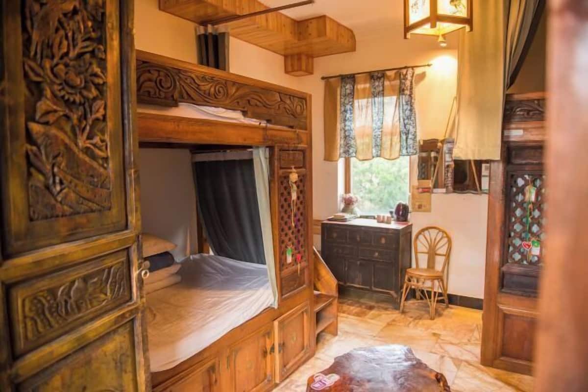 A rustic wooden room with a bunk bed, a small desk, and a chair.