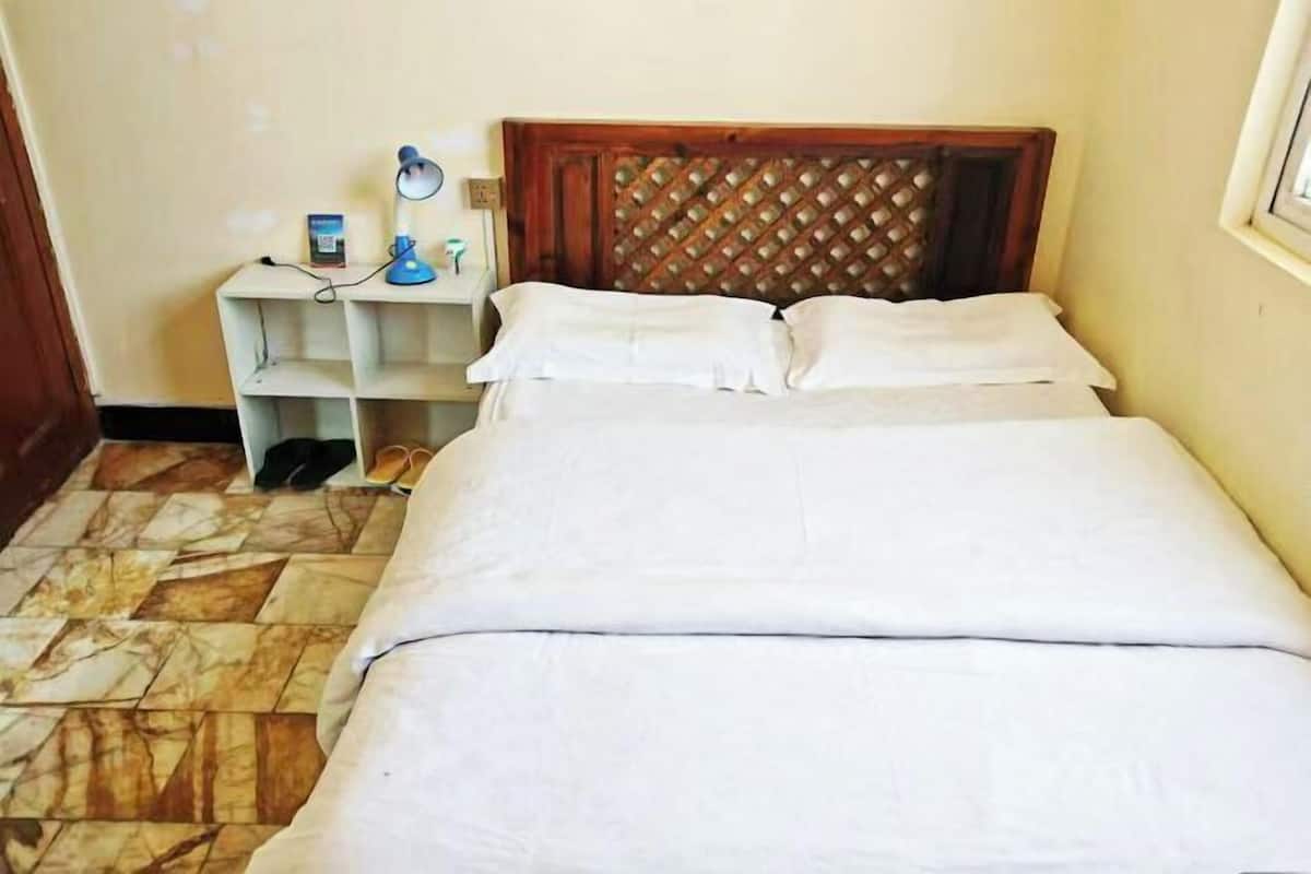 A room with a bed, a nightstand with a lamp, and a shelf with a book and a bottle.