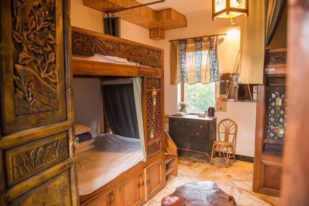 A rustic wooden room with a bunk bed, a small desk, and a chair.