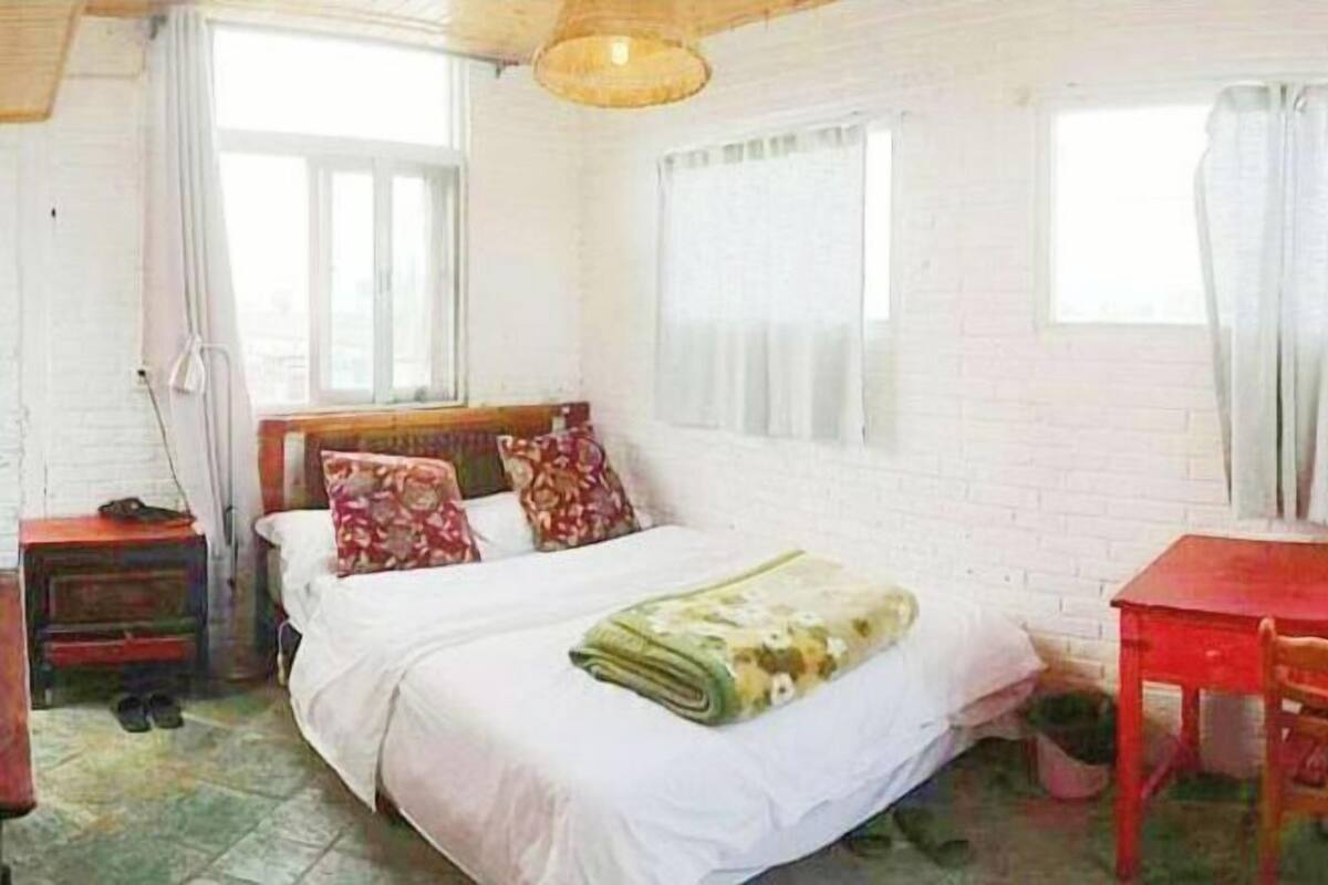 A bedroom with a bed, a wooden nightstand, a red table, and a chair.