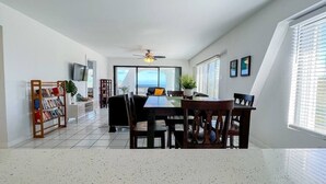 A spacious dining area with a high ceiling, a ceiling fan, and a view through large windows. - Five O'clock Somewhere Condo (Northside)