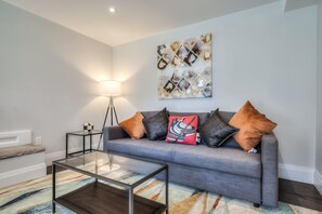 A modern living room with a grey sofa, a glass coffee table, a floor lamp, and a colorful rug.