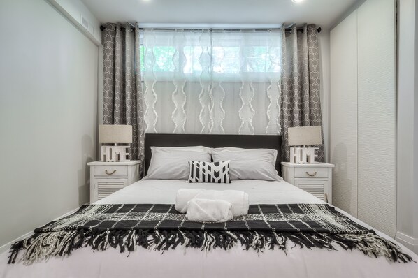 A neatly made bed with a black and white patterned blanket, two bedside tables with lamps, and a window with patterned curtains.