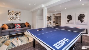 Una sala de estar moderna con mesa de ping pong, un sofá gris con cojines decorativos y arte abstracto en la pared.