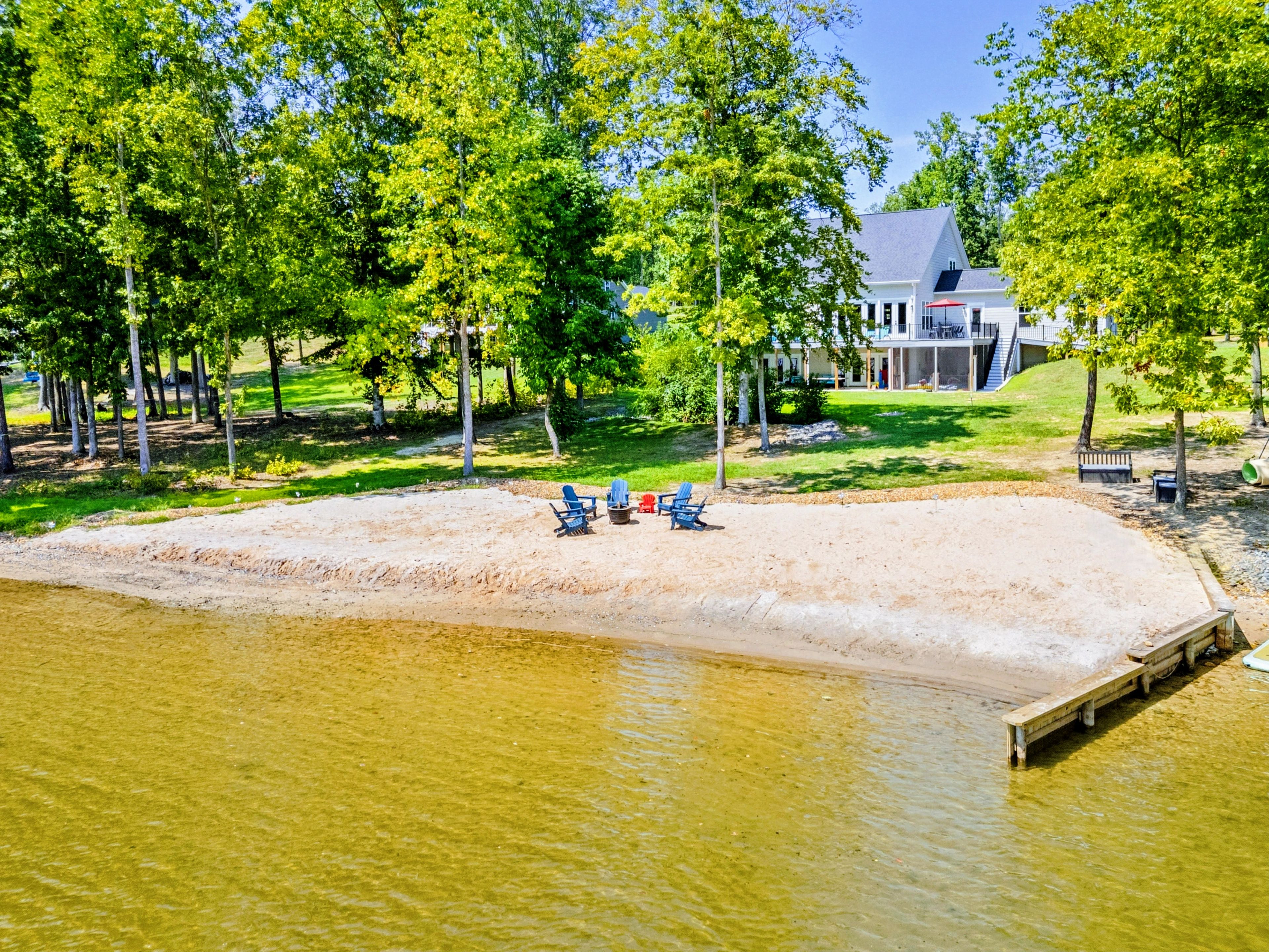 A lakeside property with a sandy beach, a dock, and a house in the background.