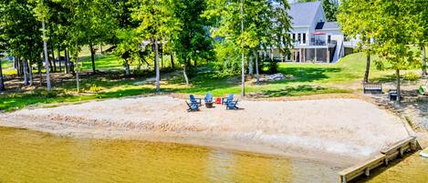 A lakeside property with a sandy beach, a dock, and a house in the background.