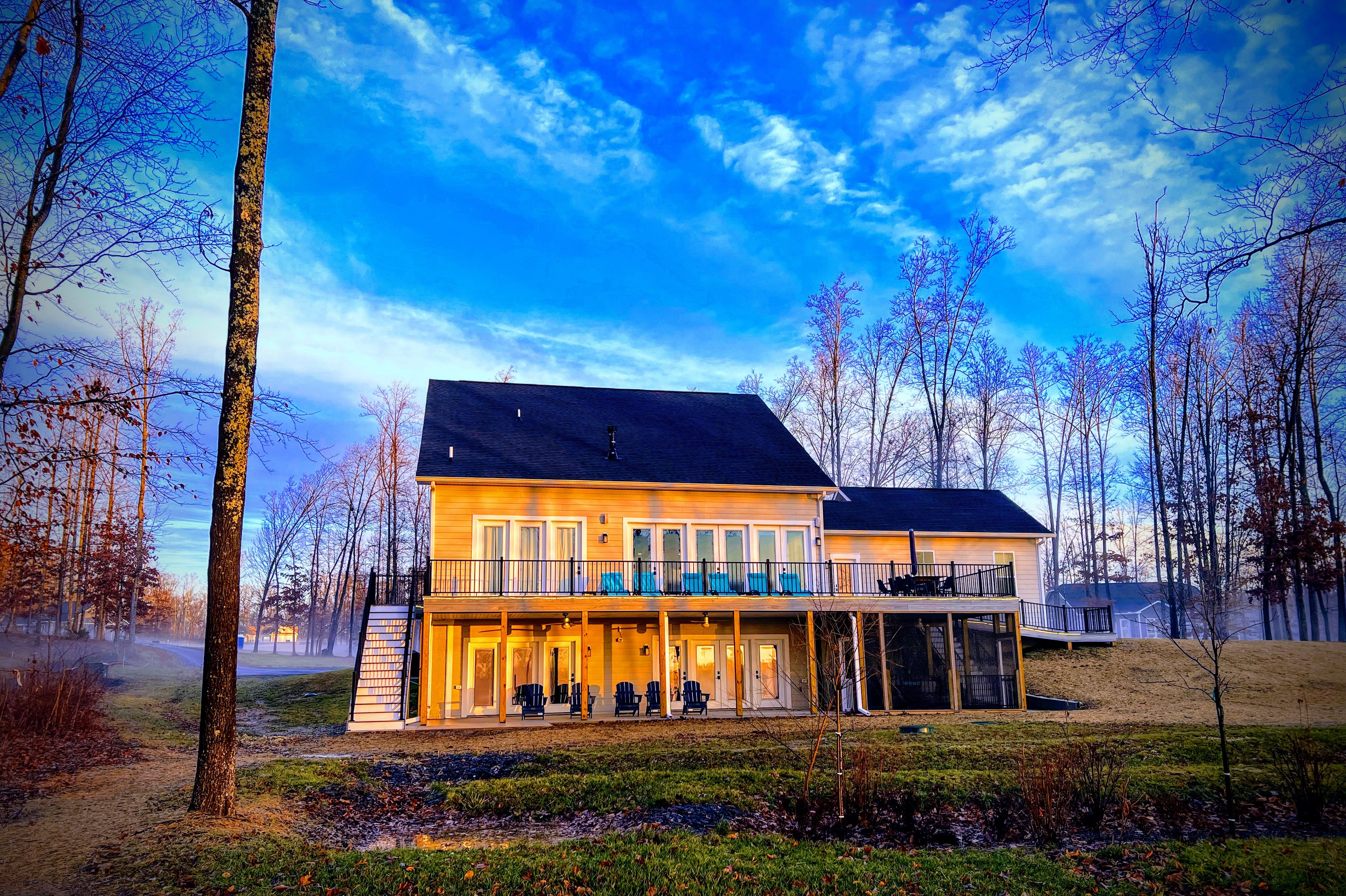 A two-story house with a balcony, a covered porch, and a view of the surrounding trees.