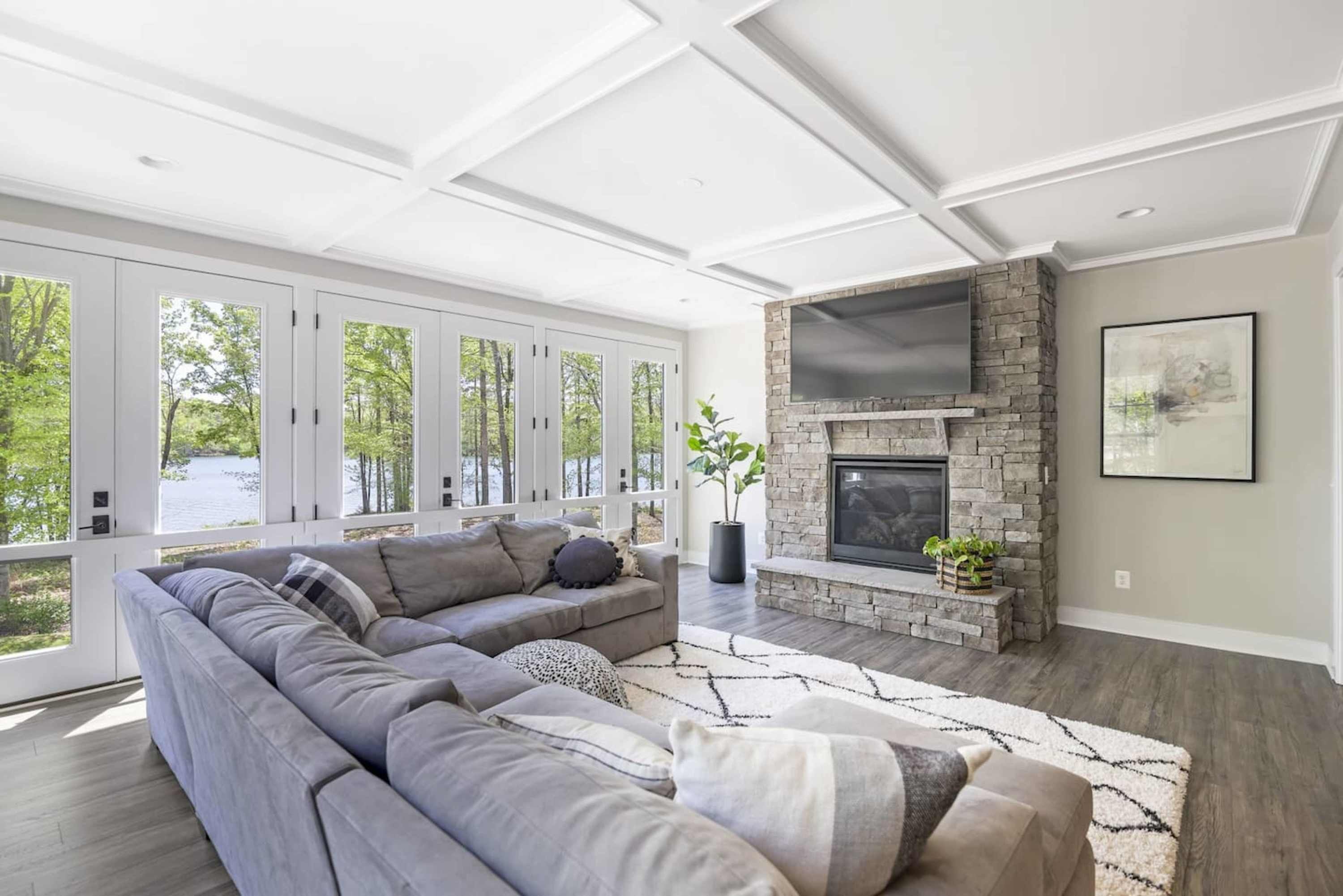 Un salon moderne avec un canapé d’angle, une cheminée et de grandes fenêtres.