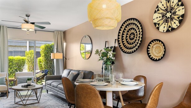 A dining area with a round table, brown chairs, and a ceiling fan. There are decorative plates on the wall and a vase with flowers on the table. - Scott Place - Amazing location, heated pool, vibrant space awaits! (Scottsdale)