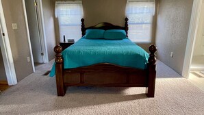 A bedroom with a wooden bed, beige carpet, and two windows with blinds. - A little bit of country (Aztec)