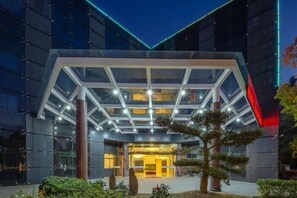 Ingresso moderno di un hotel con atrio in vetro e facciata geometrica.