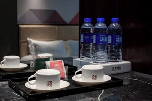 A hotel room with a bed, a tray table with cups and a water bottle, and a wall with a painting. - Borrman (hangzhou xianghu) (Hangzhou)