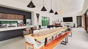 A modern kitchen with a central island, pendant lighting, and a dining area with a long wooden table and benches. - Casa Arena Volcano View Villa (Fortuna)