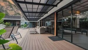 A modern outdoor patio with a wooden deck, glass walls, and contemporary furniture. - Casa Arena Volcano View Villa (Fortuna)
