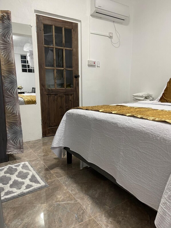 A bedroom with a bed, a wooden door, an air conditioning unit, and a patterned rug.