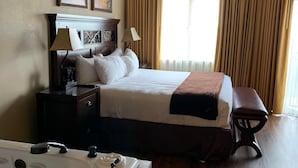 Una habitación de hotel con una cama grande, una mesita de noche, una lámpara, un ventilador de techo, una ventana con cortinas y una bañera.