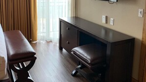 Habitación de hotel con cama, escritorio, silla, televisor montado en la pared y ventana con cortinas.