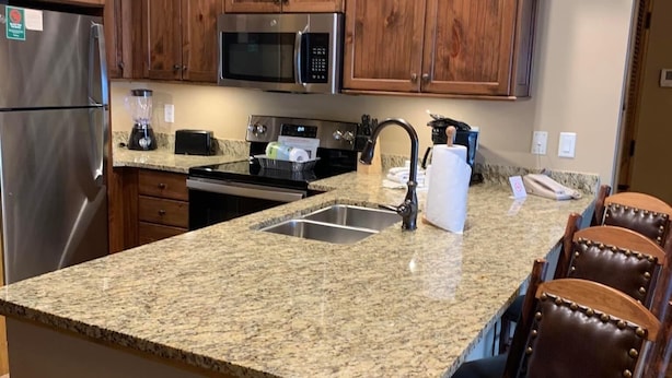 Una cocina con armarios de madera, encimeras de granito, electrodomésticos de acero inoxidable y una isla central con taburetes de bar.