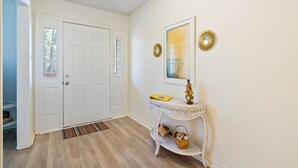 A hallway with a white door, a wicker console table with a mirror, and a striped rug.