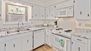 A kitchen with white cabinets, a sink, a microwave, a stove, and a window with blinds.