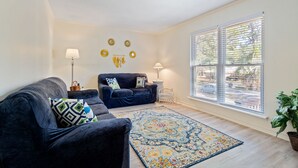 A living room with a dark blue sofa, a patterned rug, and a window with blinds.