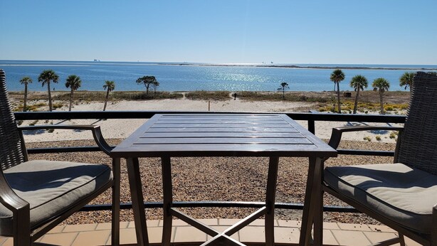 A beachside patio with a table and two chairs, overlooking a calm sea and a clear sky.