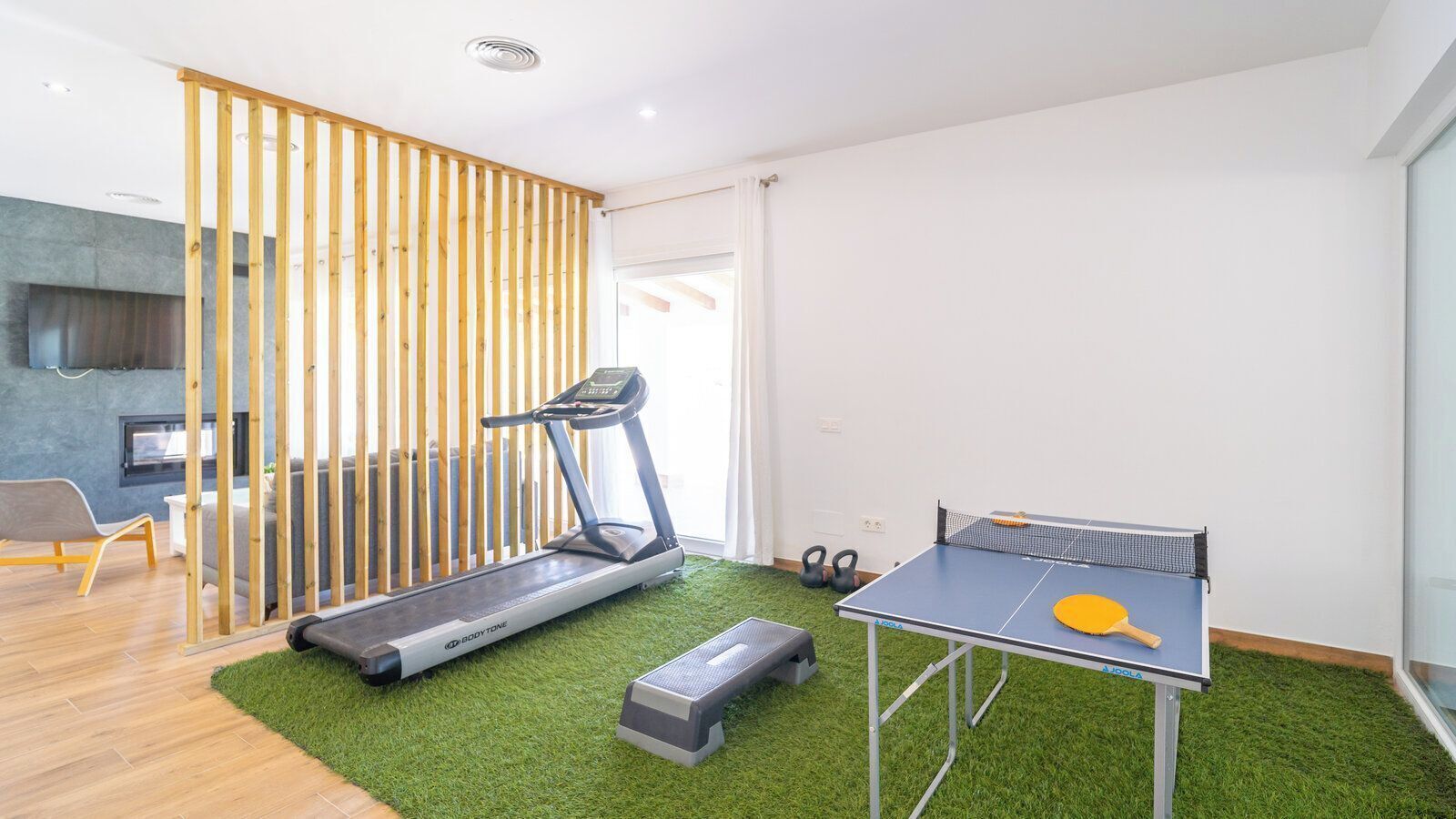 A room with a treadmill, a ping pong table, and a green artificial turf floor.