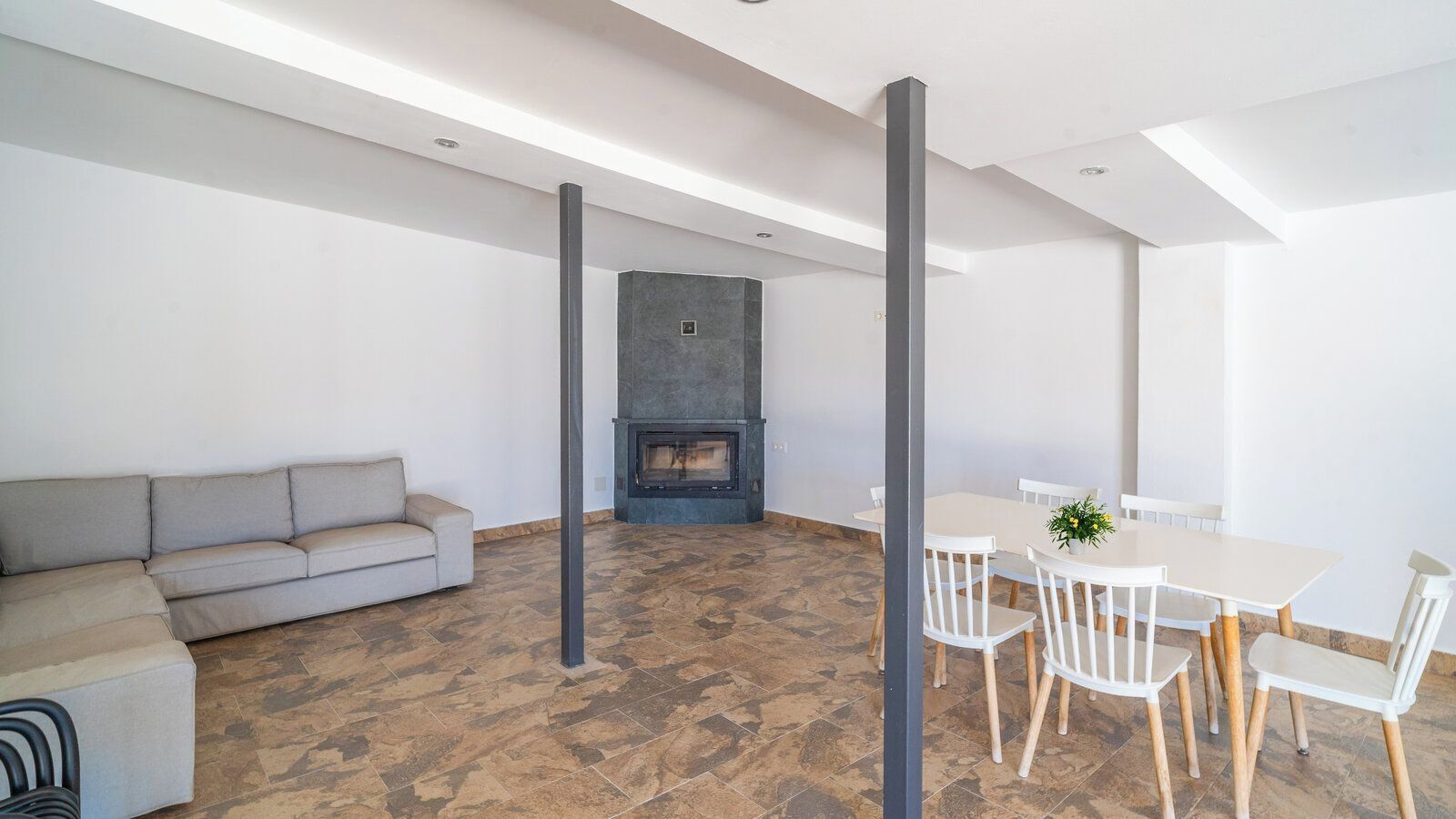 Ein modernes Wohnzimmer mit einer Couch, einem Esstisch, Stühlen, einem Kamin und freiliegenden Deckenbalken.