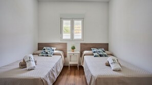 A hotel room with two beds, a small table, and a window.