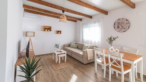 Un salon confortable avec un canapé, une table basse et une table à manger avec des chaises. Il y a une horloge au mur et une plante sur le sol.