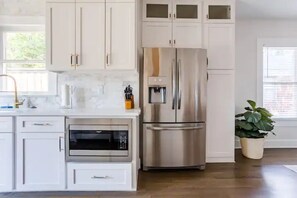 A modern kitchen with white cabinetry, stainless steel appliances, and a potted plant.