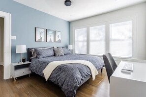 A bedroom with a bed, bedside tables, a desk, and a window with blinds.